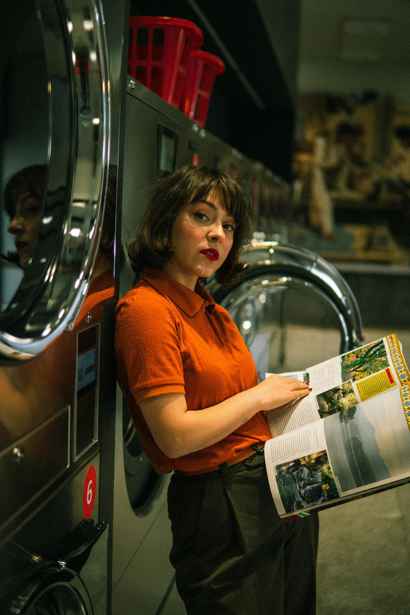 A woman reads a magazine while waiting at a modern laundromat with washing machines.