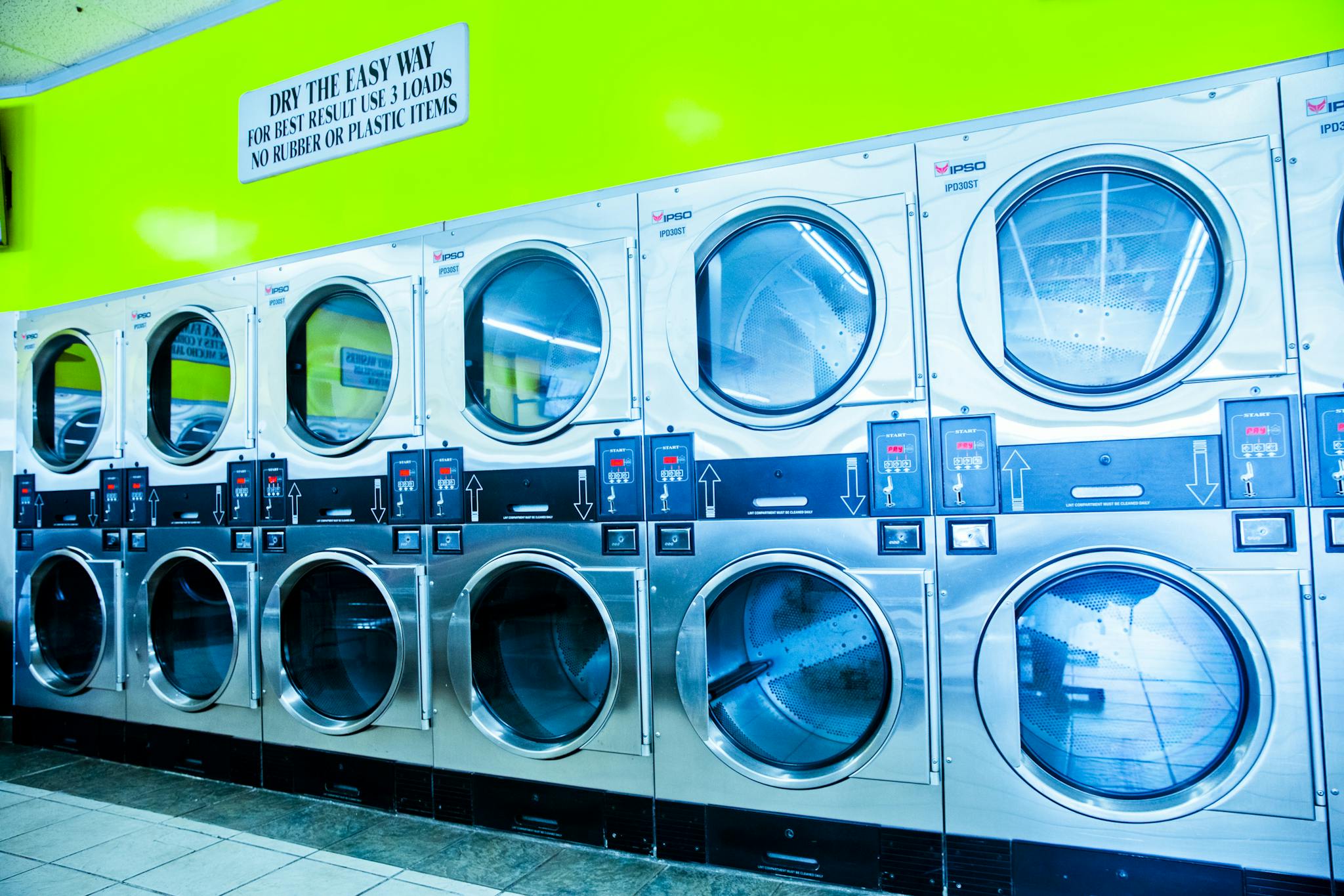 Bright modern laundromat with stainless steel industrial dryers and vibrant green wall.