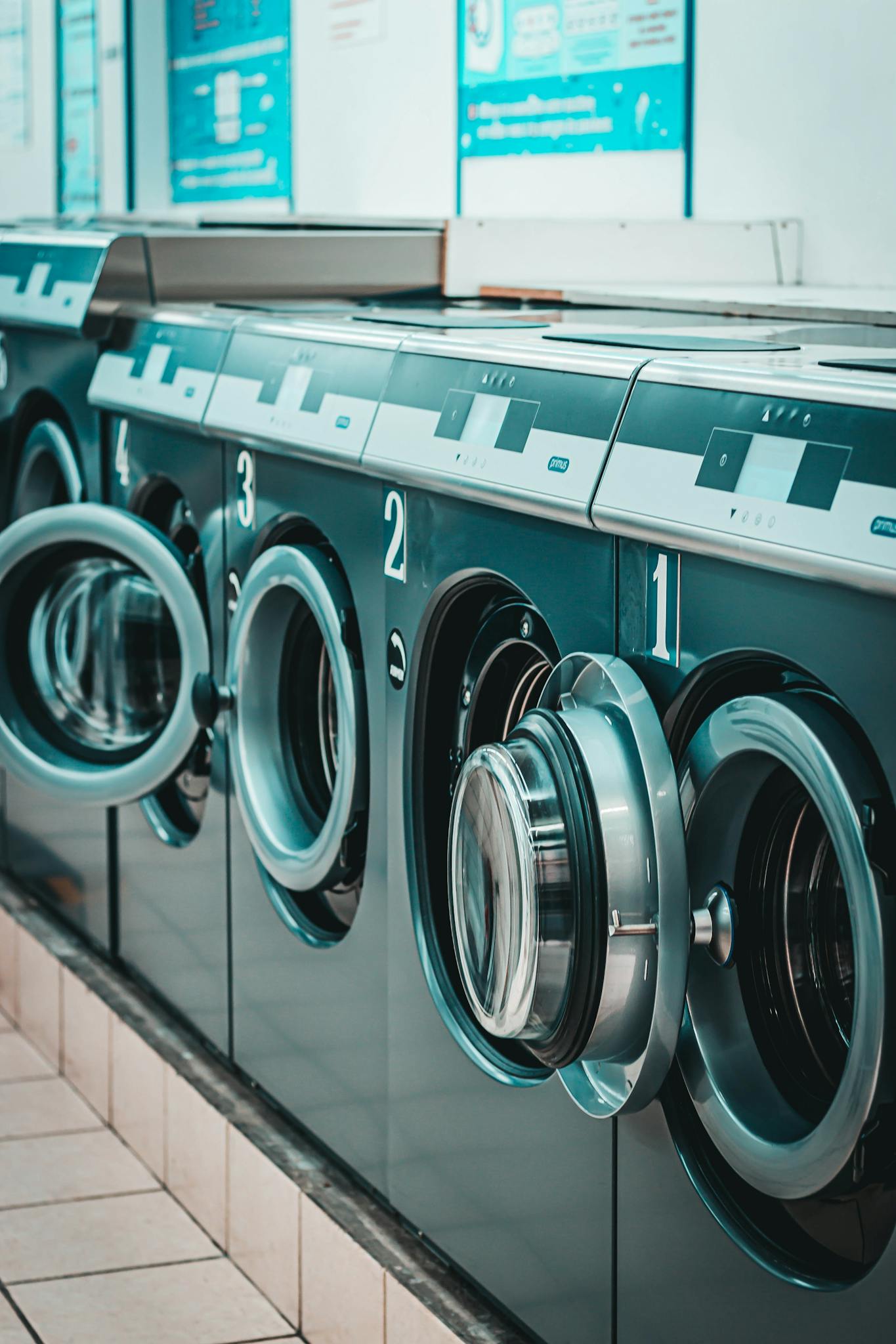 Contemporary laundromat featuring a row of stainless steel washing machines with open doors.